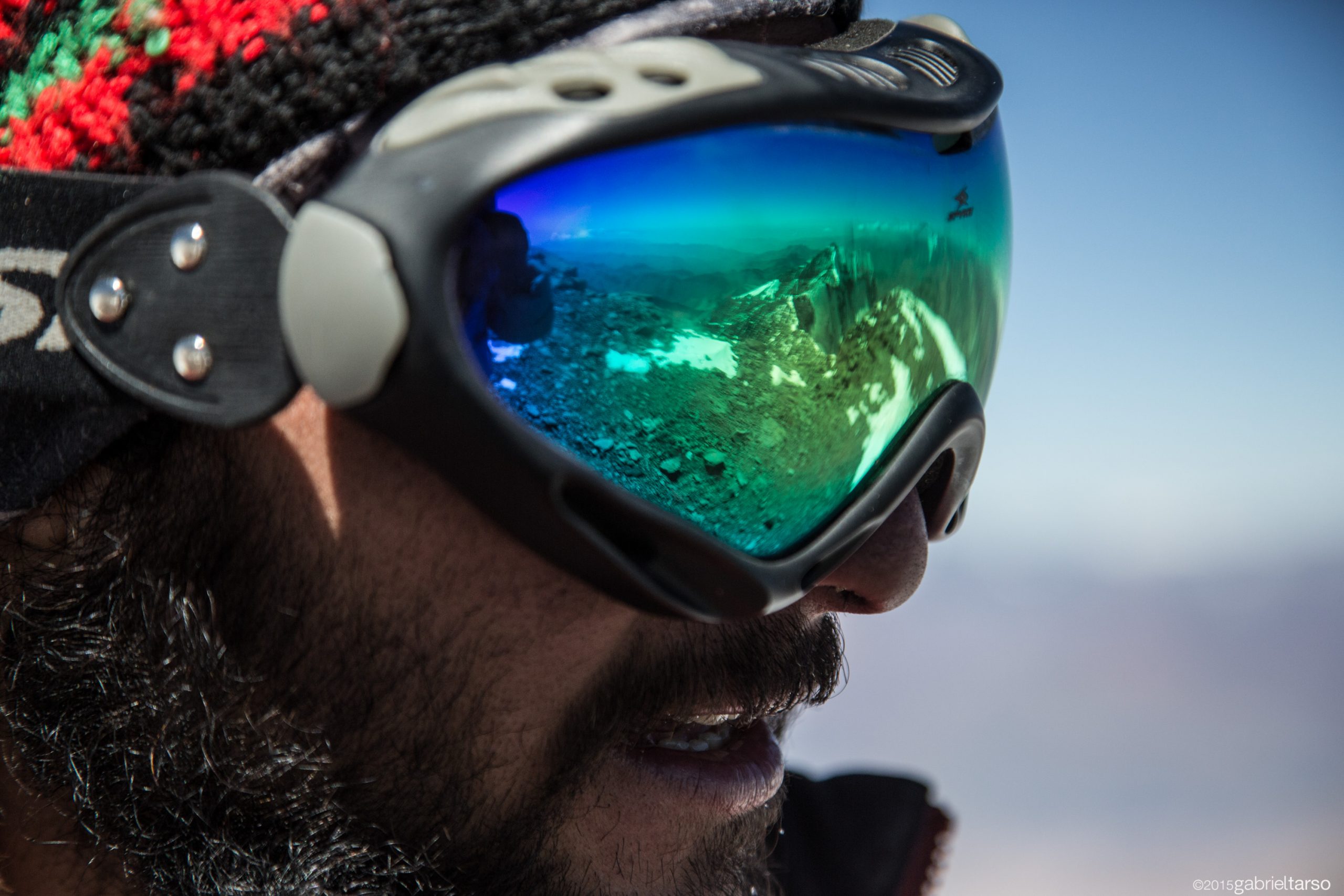 Para cégo ver: a fotografia foca o rosto de um montanhista homem usando uma viseira para proteger os olhos do reflexo da neve. 